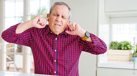 Ein älterer Man hält sich die Ohren mit seinen Fingernb zu.