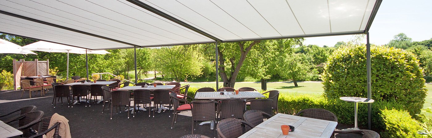 Blick auf die Terrasse eines Restaurants mit Außenbereich. Eine großes Terrassendach mit weißer Markise bietet Sonnenschutz.