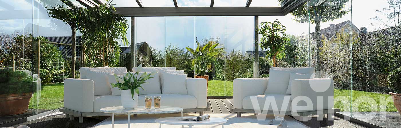 Blick in den angebauten Wohn-Terrassenbereich mit umlaufenden Glaselementen. Nach einem Regenschauer kommt die Sonne heraus.